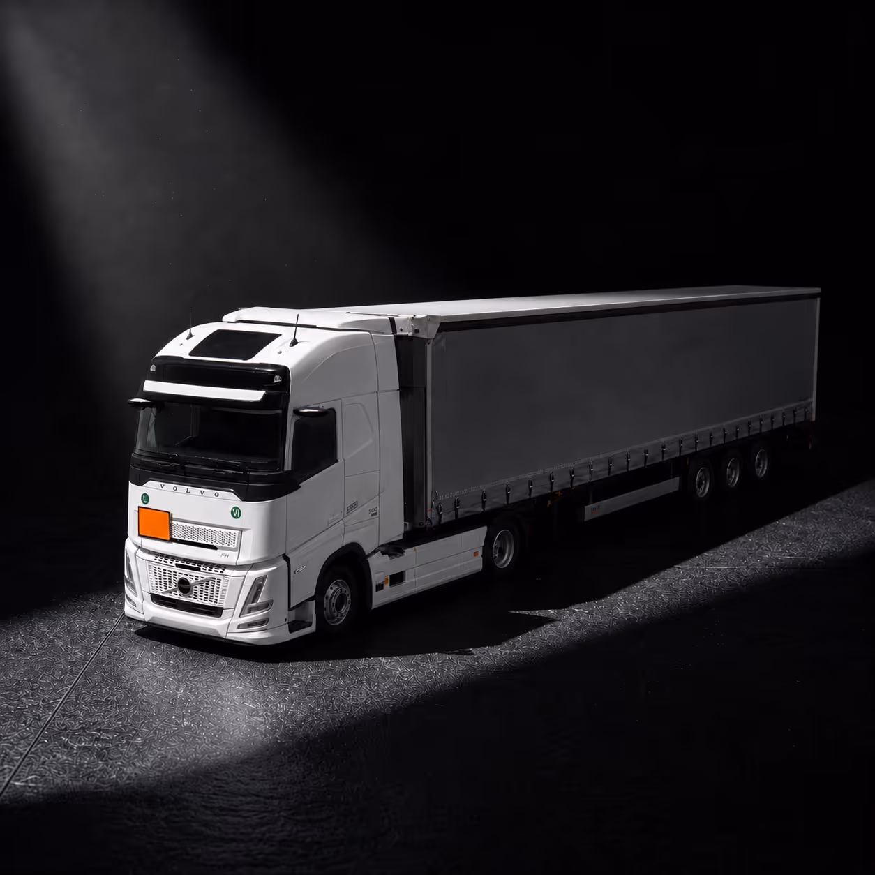 White Volvo semi truck with trailer highlighted by a spotlight on a dark textured surface with ADR plate on the front of it.