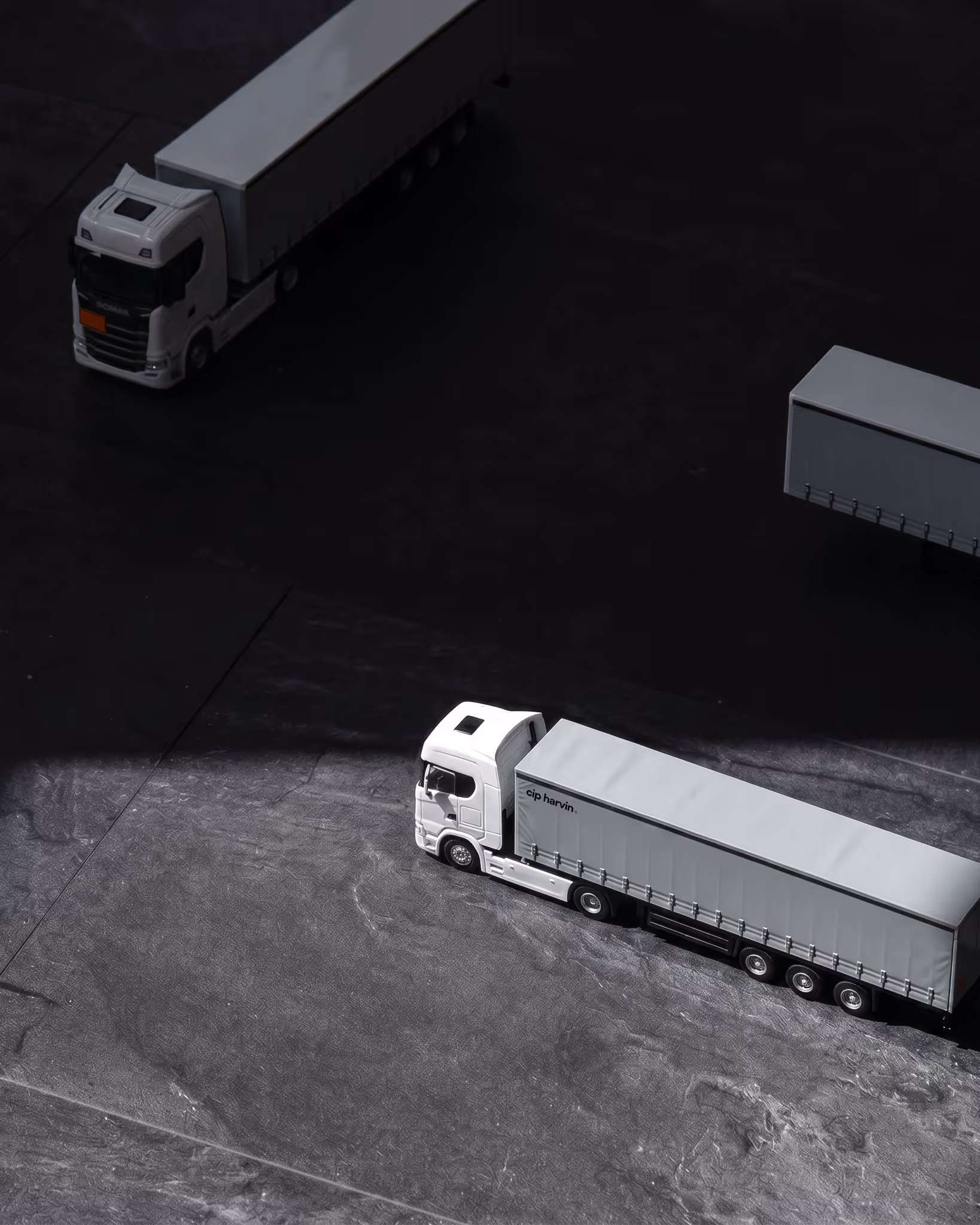 Aerial view of three white cargo trucks parked on a dark asphalt surface with shadows.